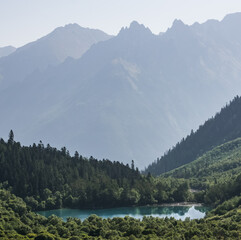 Blue mountain lake in a mountainous terrain and wooded area among coniferous trees, against the backdrop of slopes and mountain hills