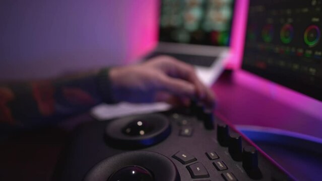 Close-up of a man's hand making edits on a special panel. Young man in glasses working on video editing on computer doing montage and color correction. Concept of creating video content.