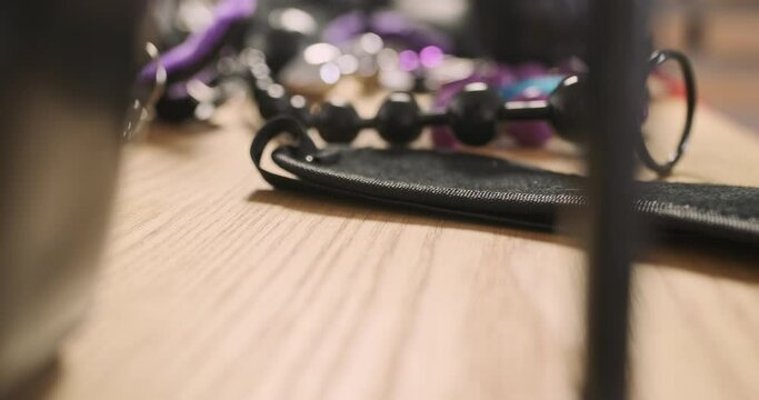 Fetish erotic items, high heels, vibrators, gags, leather bondage, butt plug rope. Side view, camera flies over the table. Preparing for sex.
