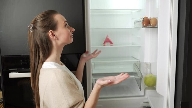 Young woman in the kitchen looks inside an empty refrigerator without food. 