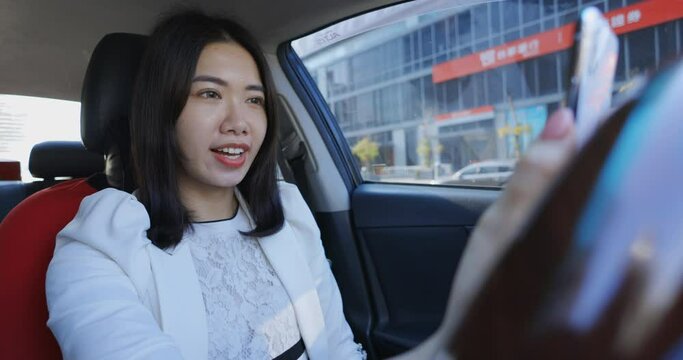 An Asian businesswoman is using her mobile phone inside the car to make a video call with colleagues or clients, demonstrating her flexibility and adaptability in conducting business remotely.	
