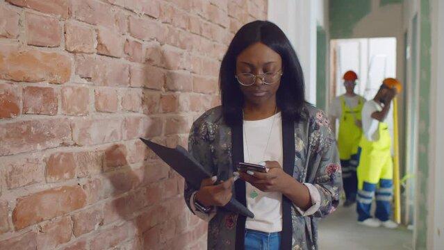 African-American woman designer use smartphone at construction site. Realtime