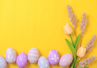 Happy Easter holiday greeting card design concept. Colorful Easter Eggs and spring flowers on yellow background. Flat lay, top view, copy space.
