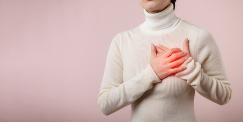 Young woman suffering from heart attack on light pink studio background. Painful cramps, Heart disease, Pressing on chest with painful expression. Healthcare world health day concept.