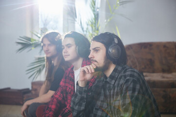 Three men with mobile phones and headphones enjoy music at home. A group of three young people feeling free, enjoying life
