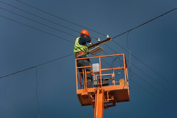 Worker on cherry picker install led lantern on electric wires at height on city street. Man in lift...