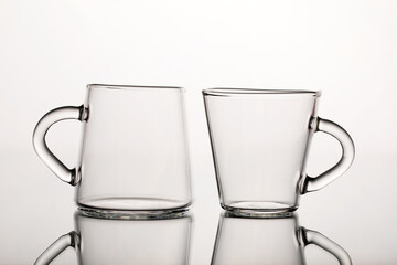 Two glass cups for coffee on a mirror surface and a white background.