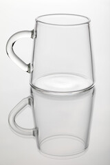Glass cup for coffee on a mirror surface and a white background.