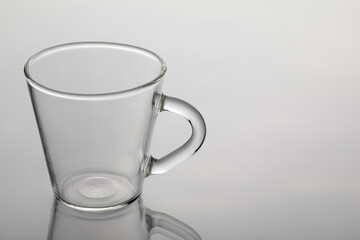 Glass cup for coffee on a mirror surface and a white background.