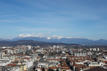 Panoramic city view of Ljubljana, Slovenia with snow on top of mountains on sunny day.