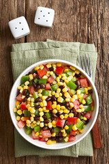 Mexican style colorful fresh vegetable salad made of beans, corn, tomato and bell pepper served in bowl, photographed overhead on wood (Selective Focus, Focus on the salad)