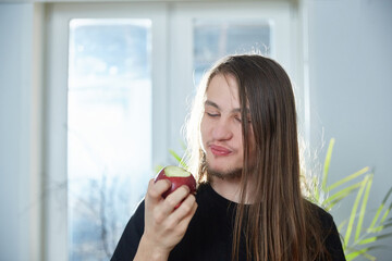 Hippie guy with long hair eats an apple at home