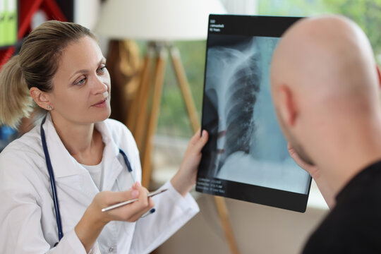 Female doctor holding x-ray image and pen in hands and speaking with male patient.