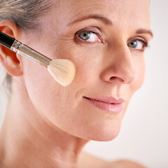 Brightening up her complexion. Closeup studio shot of an attractive mature woman applying makeup...