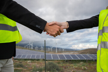 Two business people shaking hands at a solar farm, female and male managers