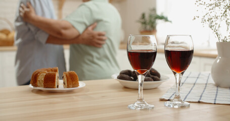 Cute senior asian couple are celebrating their anniversary, drinking wine, listening to music and dancing in their kitchen, relaxing after retirement - pension, old couple in love 