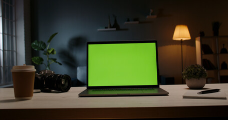 Modern laptop with template copy space green screen set on table in living room at home at night for distant learning or remote work green screen template