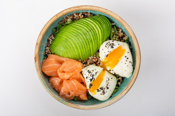 Poke bowl with quinoa, salmon, avocado and two poached eggs. Round blue ceramic bowl isolated on white background. Yolks spread Top view.