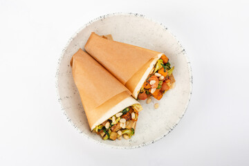 2 vegetarian rolls with carrots, broccoli, tofu, tomatoes, zucchini, pine nuts on a round white plate on a white background. Top view.