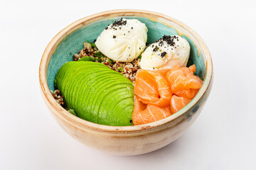 Poke bowl with quinoa, salmon, avocado and two poached eggs. Round blue ceramic bowl isolated on white background. Close up 3/4.