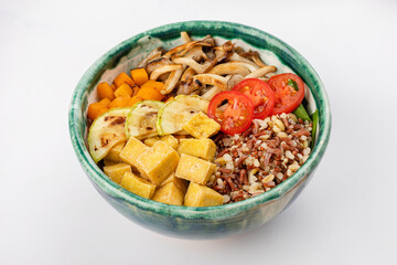 Vegetarian poke bowl with quinoa, brown rice, tofu, oyster mushrooms, carrots, zucchini, cherry tomatoes. Round green bowl on a white background. Close up 3/4