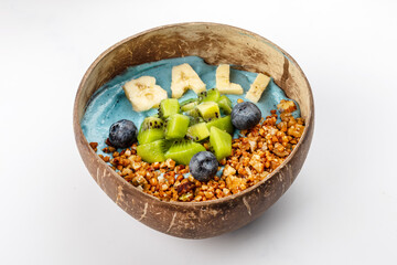 Summer blue smoothie bowl with yogurt, kiwi, blueberries, banana lettering Bali, nuts and buckwheat. A plate of coconut on a white background. Close up 3/4