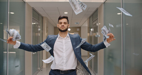 Caucasian man with arrogant face is standing in office hall throwing money in air, celebrating his...