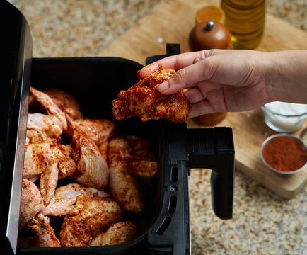 woman hand placing a chicken wing on an air fryer