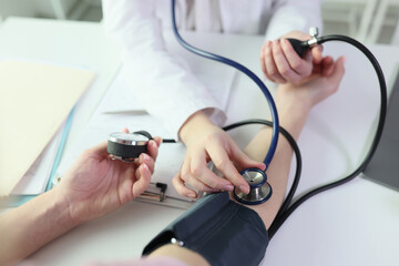 Doctor measures patient's blood pressure using sphygmomanometer and stethoscope.