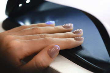 Woman drying nails in lamp. Client with beige varnish at manicure salon carefully waiting when her nails become dry in UV light. Closeup shoot 