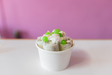 Close up of a rolled ice cream decorated with green bubbles and yogurt toppings