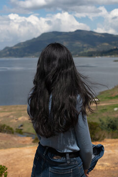 mujer de pelo largo negro de espaldas mirando hac&iacute;a paisaje de lago y monta&ntilde;as 