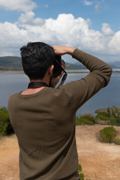 hombre tomando fotografía con cámara fotográfica a paisaje de lago con montañas, vertical  