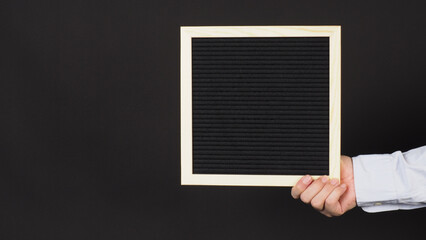 Hand is holding a black letter board on black background.