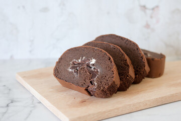 Chocolate roll cake slice with vanilla cream and dark compound chocolate. Sweets dessert cream roll chocolate snacks and food concept. Swiss Roll Cake, Cake roll on wooden
