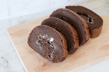 Chocolate roll cake slice with vanilla cream and dark compound chocolate. Sweets dessert cream roll chocolate snacks and food concept. Swiss Roll Cake, Cake roll on wooden