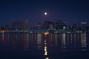 Fototapeta premium Tokyo skyline under full moon. Night photo with the modern skyscraper office buildings in Tokyo and Rainbow Bridge.