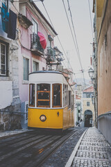 a yellow vintage hill tram driving up a steep street in the city Lisbon in Portugal