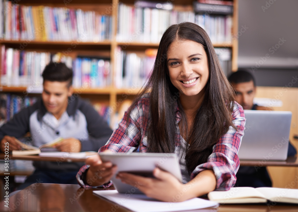 Poster getting down to some studying. portrait of an attractive female student using her digital tablet dur