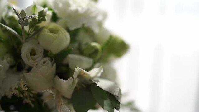 White bouquet of flowers stands in a vase on a table by the window