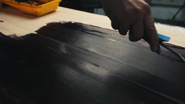 Coloring with varnish impregnat of wooden table using roller brush. Black color painting or varnishing wooden surface. House and furniture renovation.