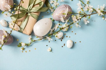 beautiful light easter layout with eco-wrapped gifts, golden and marble eggs, cherry blossoms and confetti on a pastel blue background. top view. copy space. flat lay. place for text