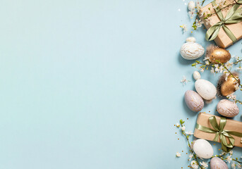 beautiful light easter layout with eco-wrapped gifts, golden and marble eggs, cherry blossoms and confetti on a pastel blue background. top view. copy space. flat lay. place for text