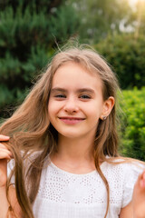 cute little girl in a white dress has smiling and straightening her wind-blown hair a walk in the garden in a summer green park