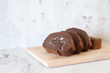Chocolate roll cake slice with vanilla cream and dark compound chocolate. Sweets dessert cream roll chocolate snacks and food concept. Swiss Roll Cake, Cake roll on wooden
