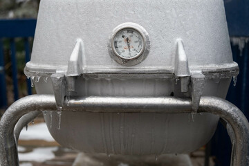 Grill with temperature gauge covered in ice after a winter storm; summertime dreaming of grilling