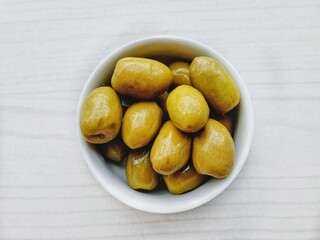  green olives in white pot and light wooden background