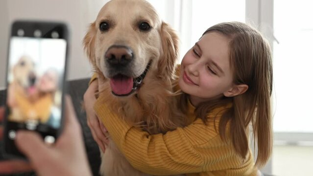 Girl hand with smartphone taking photo of golden retriever dog and preteen child kid at home. Woman mother photograph shoting pet doggy and daughter with mobile phone camera