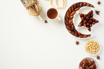 Ramadan Kareem greeting card design. Flat lay, top view dried dates in islamic star and crescent plate, nuts, oriental lantern, cup of tea.