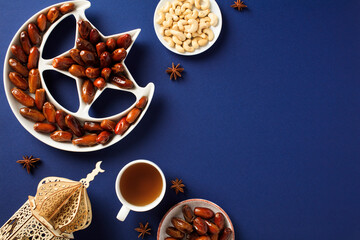 Islamic star and crescent plate with dried dates, nuts, drink, wooden oriental lantern on dark blue...